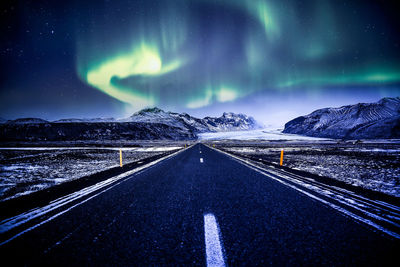 Road amidst snowcapped mountains against sky at night