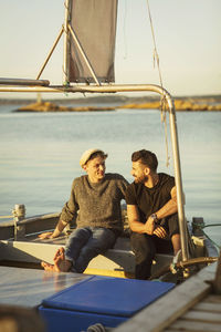 Young male friends talking while sitting on boat at harbor