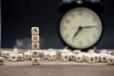 Close-up of sorry text made with toy blocks against alarm clock on wooden table