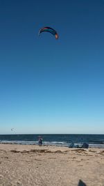 Man paragliding at beach against clear blue sky