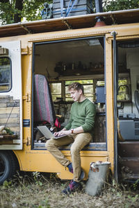 Full length of man using laptop in caravan while camping at forest