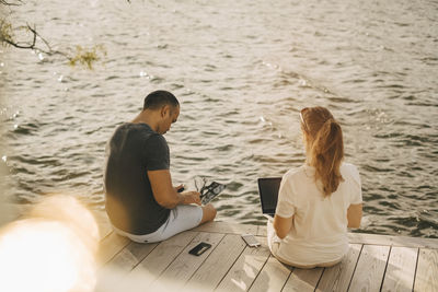 Mature couple using laptop while sitting on patio against lake during summer vacation