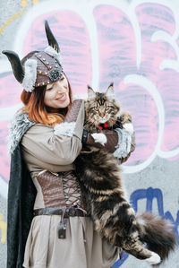 Woman in costume holding cat against graffiti