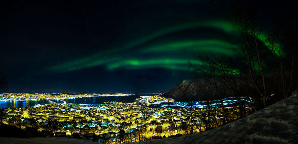 Illuminated city aurora borealis in sky at night