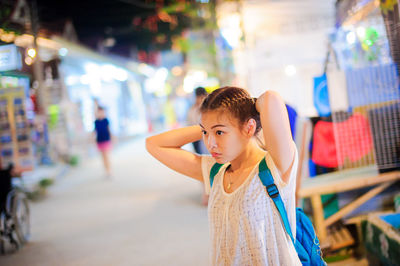 Young woman tying hair while standing in market at night