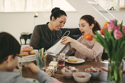 Surprised girl looking at bag while sitting with mother during meal in birthday party