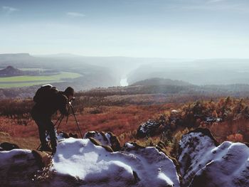 Professional photographer takes photos with camera and tripod on snowy peak. spring valley below