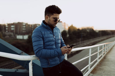 Young man using mobile phone against sky