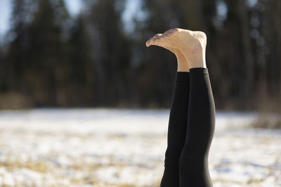 Close-up of legs bare foot of young attractive woman practicing yoga on snowy field