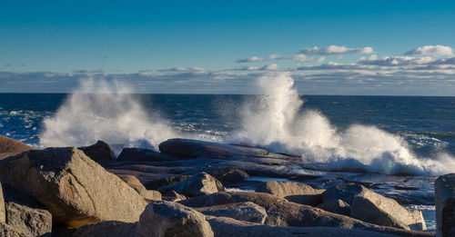 Waves splashing on rocks at shore against sky