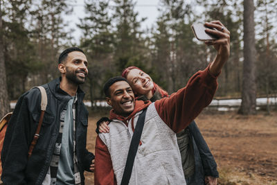 Happy multiracial friends taking selfie with smart phone in yard