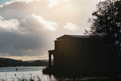 Building by lake against sky during sunset