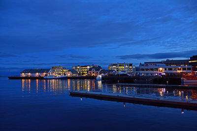 Illuminated buildings by sea against blue sky at dusk