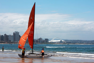 People on sea by city against sky