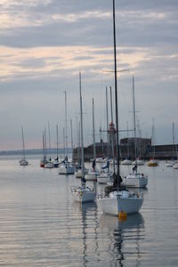 Sailboats moored on sea against sky during sunset