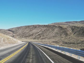 Empty road by mountain against clear blue sky