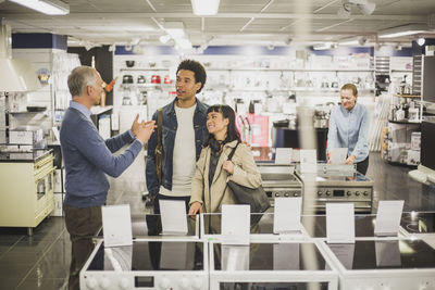 Mature owner talking to smiling female and male customers in electronics store