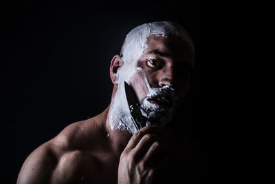 Man shaving with knife against black background