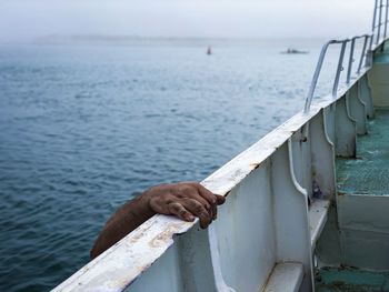 Cropped hand of man climbing on ship in sea