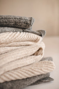 Stack of knitted wool textile sweaters clothes on white blanket in bed at home room close up.