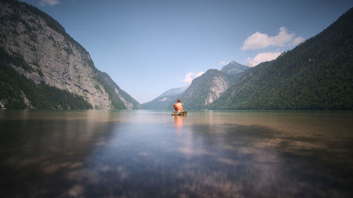 Boy sitting on lake against sky and mountains