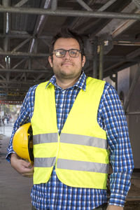 Construction worker wearing a yellow safety vest posing carrying his yellow helmet underarm