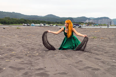 Woman playing with sand at beach against sky