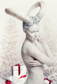 Side view of naked young woman wearing horns while standing by gift boxes