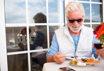Smiling senior man drinking wine and eating food on table 