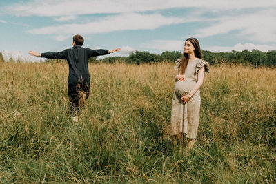 Pregnant woman with boyfriend running on grassy field