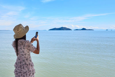 A woman using mobile phone taking photo at sea