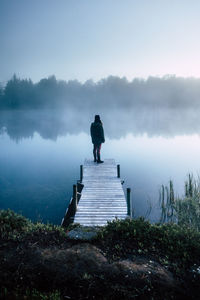 Rear view of woman standing on pier over lake against sky