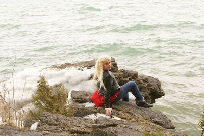 Portrait of transgender male sitting on rocks by sea