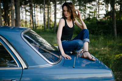 Young hipster woman sitting on a blue vintage car.