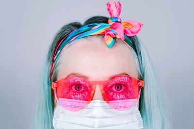 Close-up portrait of woman wearing hat mask and sunglasses against white background