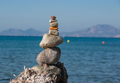 Stack of stones on rock by sea against sky