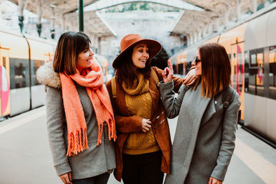 Happy friends standing on station in city