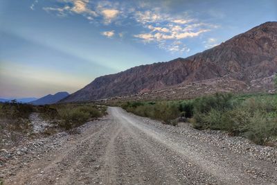 Dirt road along landscape and mountains against sky