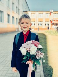 Portrait of boy with pink flower in front of building