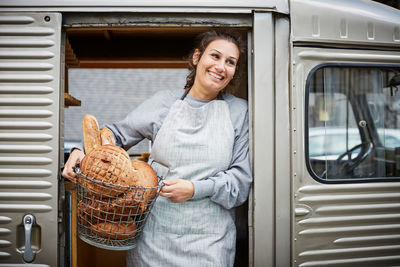 Smiling saleswoman carrying basket of fresh breads in food truck