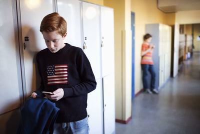 High school student using mobile phone by locker