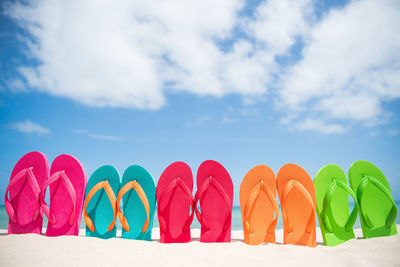 Close-up of colorful flip-flops at beach against sky