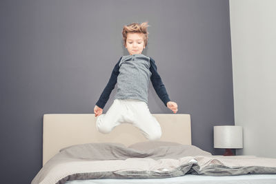 Low angle view of boy jumping on bed at home