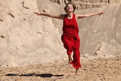 Full length of happy young woman with arms raised on beach