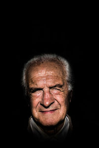 Portrait of smiling senior man against black background