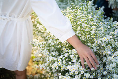 Midsection of woman standing by white flowering plants