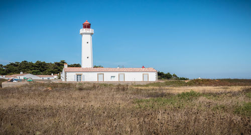 Lighthouse on field by building against clear blue sky