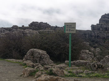 Road sign by rocks against sky