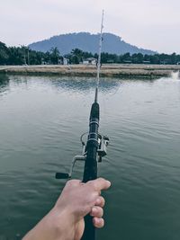 Cropped hand of person holding fishing rod by lake
