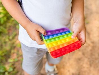 Little boy plays square rubber fidget toy pop it. rainbow-colored anti stress tactile toy.